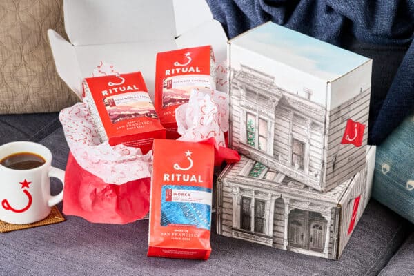 Mug filled with coffee next to 3 bags of drip coffee in gift box with tissue paper