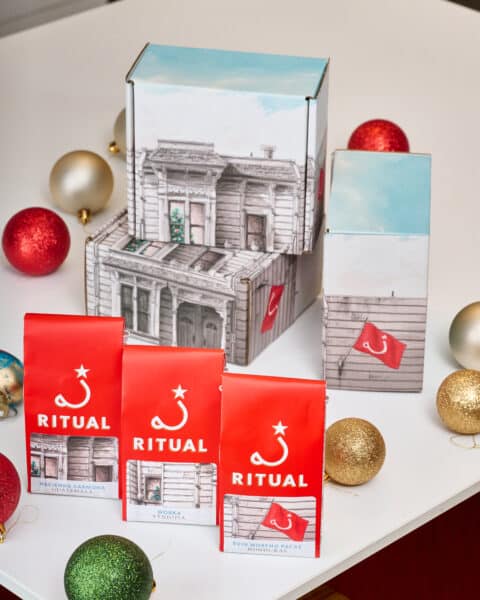 Three 4-ounce bags of drip coffee in front of gift boxes on a white table surrounded by circular ornaments.