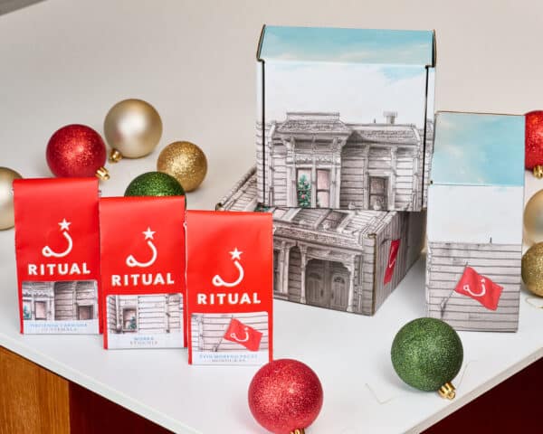 Three 4-ounce bags of drip coffee in front of gift boxes on a white table surrounded by circular ornaments.