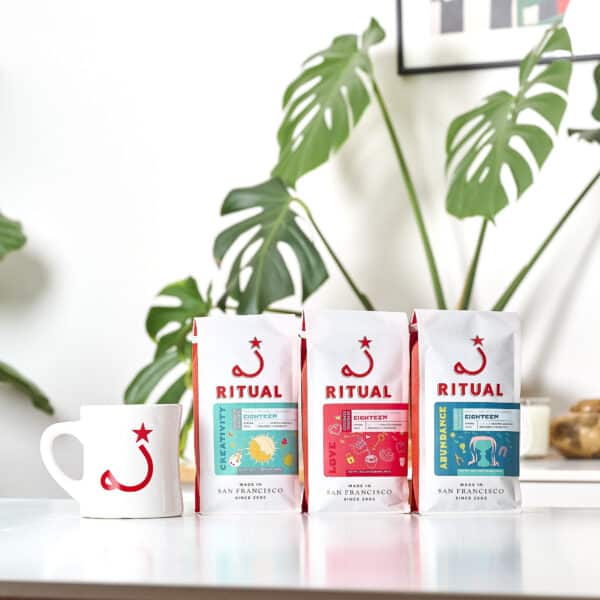 Mug and 3 espresso bags on table with plant in the background
