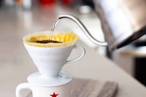 Silver kettle streaming water into a ceramic V60 filled with coffee grounds