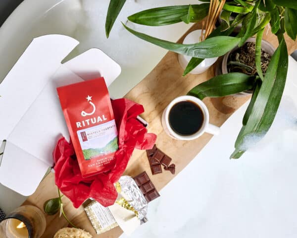 Bag of of Ritual coffee in a box with red tissue paper on a wooden plank with pieces of Dandelion Chocolate.