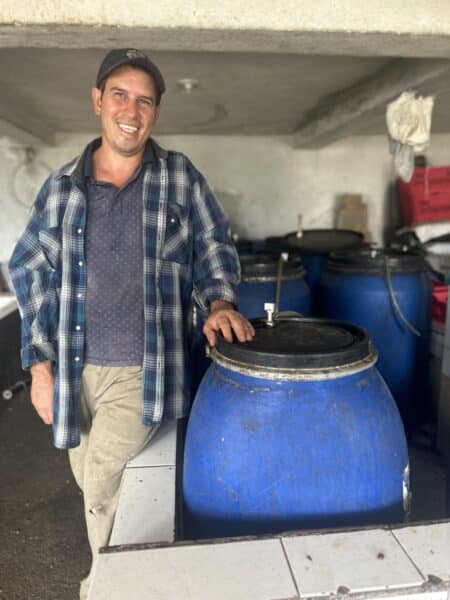 Evin Moreno with left hand on blue fermentation bucket