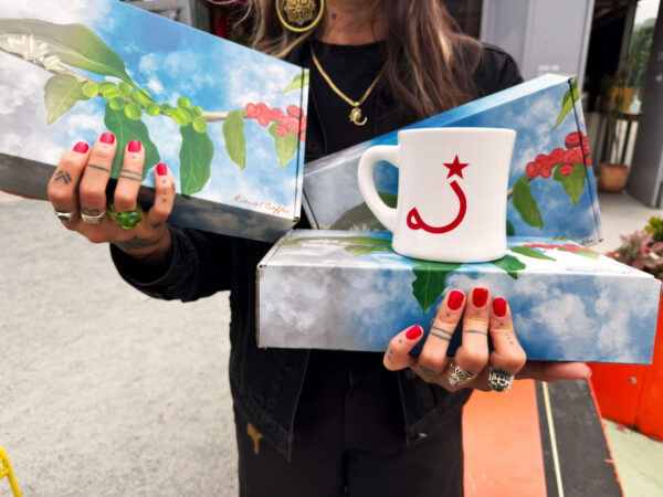 Person holding 3 boxes with a coffee mug on top