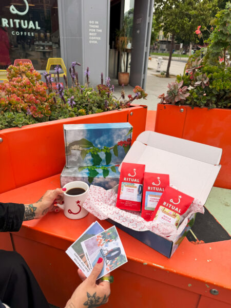 Hands holding coffee mug and art prints on red table.