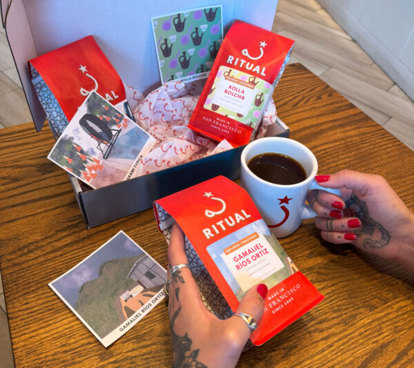 Box with 2 bags of coffee. Hand holding one coffee bag and mug in the other.