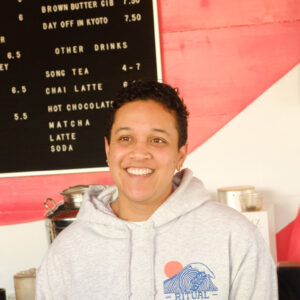 Staff member Allissia at the counter in front of the cafe menu